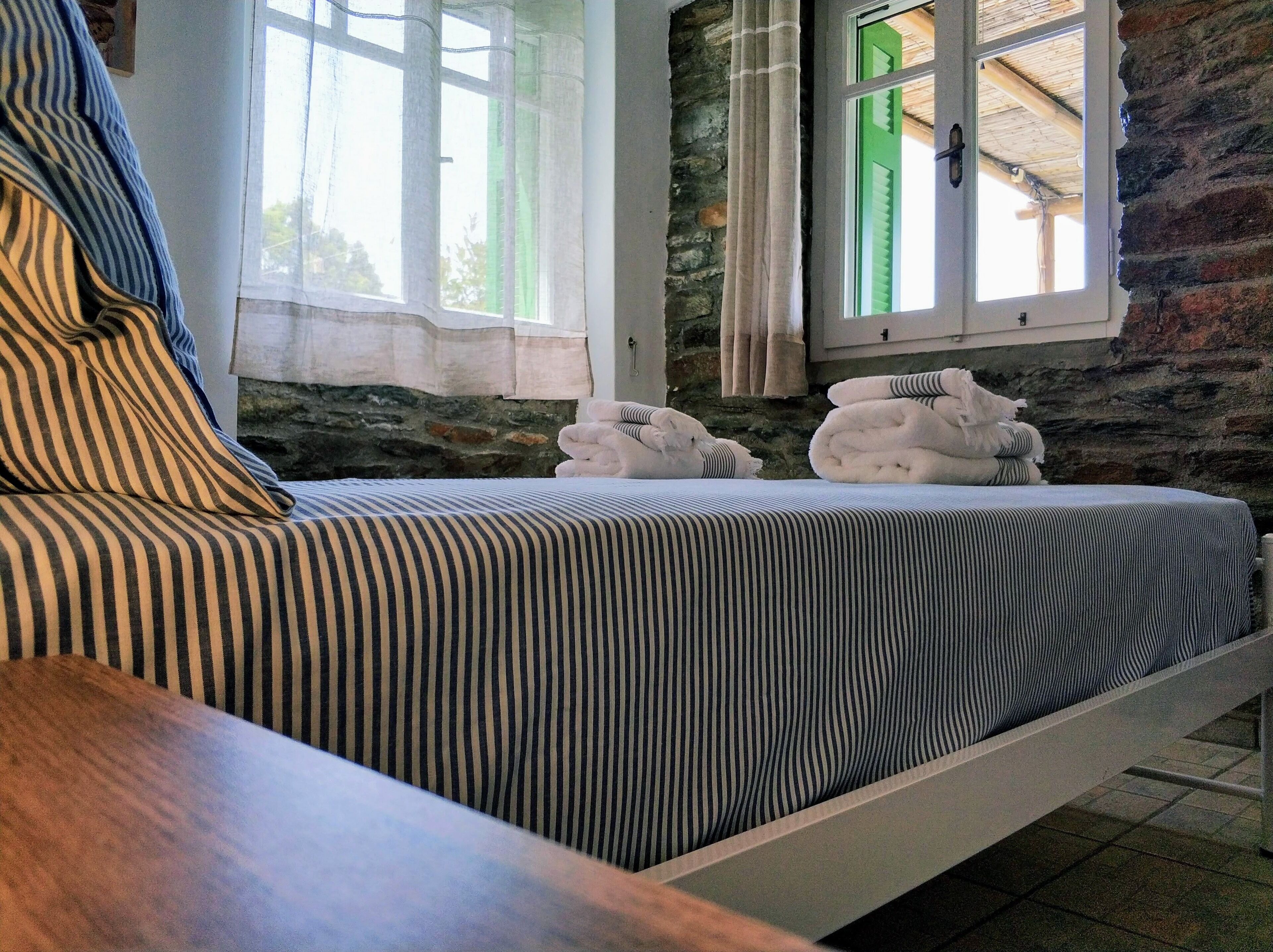 A bed with striped bedding, a stone wall, and a window with curtains.
