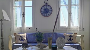 A room with a blue sofa, decorative pillows, a table with various items, and a wall clock.
