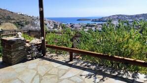 A stone-paved terrace with a wooden railing, overlooking a coastal town with buildings and a clear blue sky.
