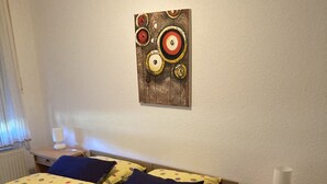 Een slaapkamer met een bed, nachtkastje, lamp en een kunstwerk aan de muur.