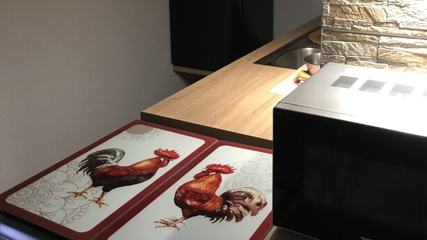 Een keuken met een houten aanrecht, een fornuis met een haan ontwerp, een zwarte magnetron en een betegelde achterwand.