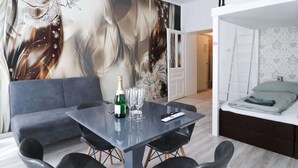 Un salon moderne avec un canapé gris, une table à manger en verre et quatre chaises, ainsi qu’un grand tableau abstrait accroché au mur.