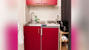 Une cuisine de taille réduite avec des meubles de rangement rouges, un évier en acier inoxydable et une machine à café posée sur une étagère.