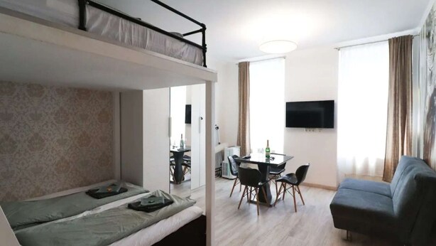 Une pièce compacte comprenant un lit superposé, un coin repas avec une table et des chaises, un canapé et un téléviseur fixé au mur.