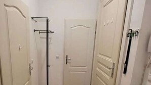 Un couloir étroit avec un parquet en bois disposé en chevrons, des portes blanches et un radiateur sur le côté gauche.