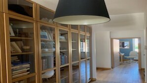 A hallway with a wooden bookshelf filled with books and decorative items, leading to a room with a white chair and a desk. - Downtown Toulouse house with pool (Toulouse)