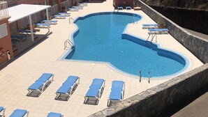 Un hotel con una piscina grande rodeada de sillones de descanso, vista despejada del océano y un letrero que muestra apoyo a Ucrania.