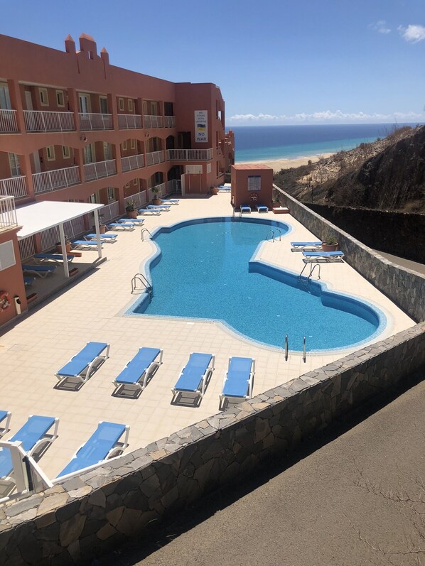 Ein Hotel mit einem großen Pool, umgeben von Liegestühlen, und einem uneingeschränkten Blick auf den Ozean. Ein Schild zeigt Unterstützung für die Ukraine.