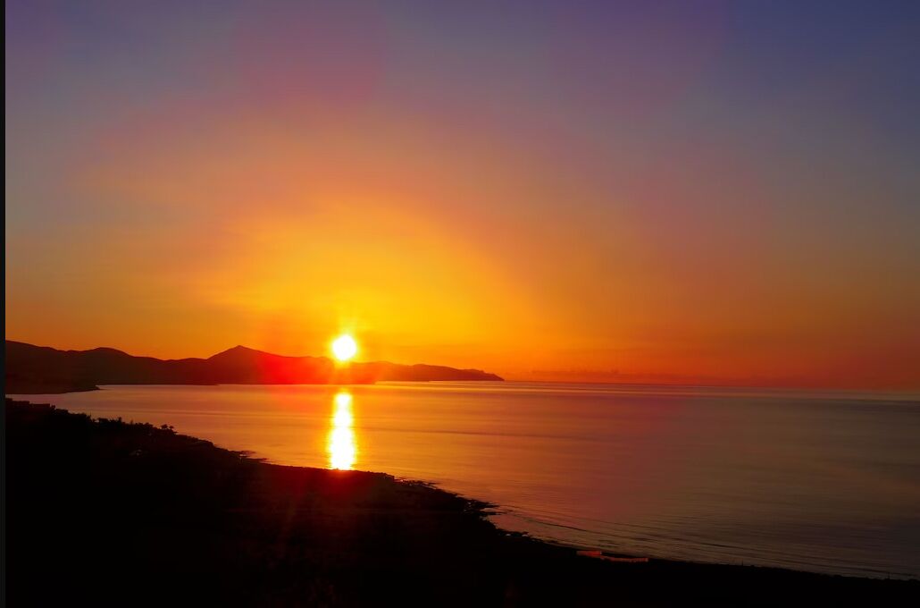 A sunset over a calm sea with a distant shoreline.