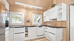 Une cuisine moderne avec des murs recouverts de panneaux en bois, des meubles blancs et un plan de travail noir.