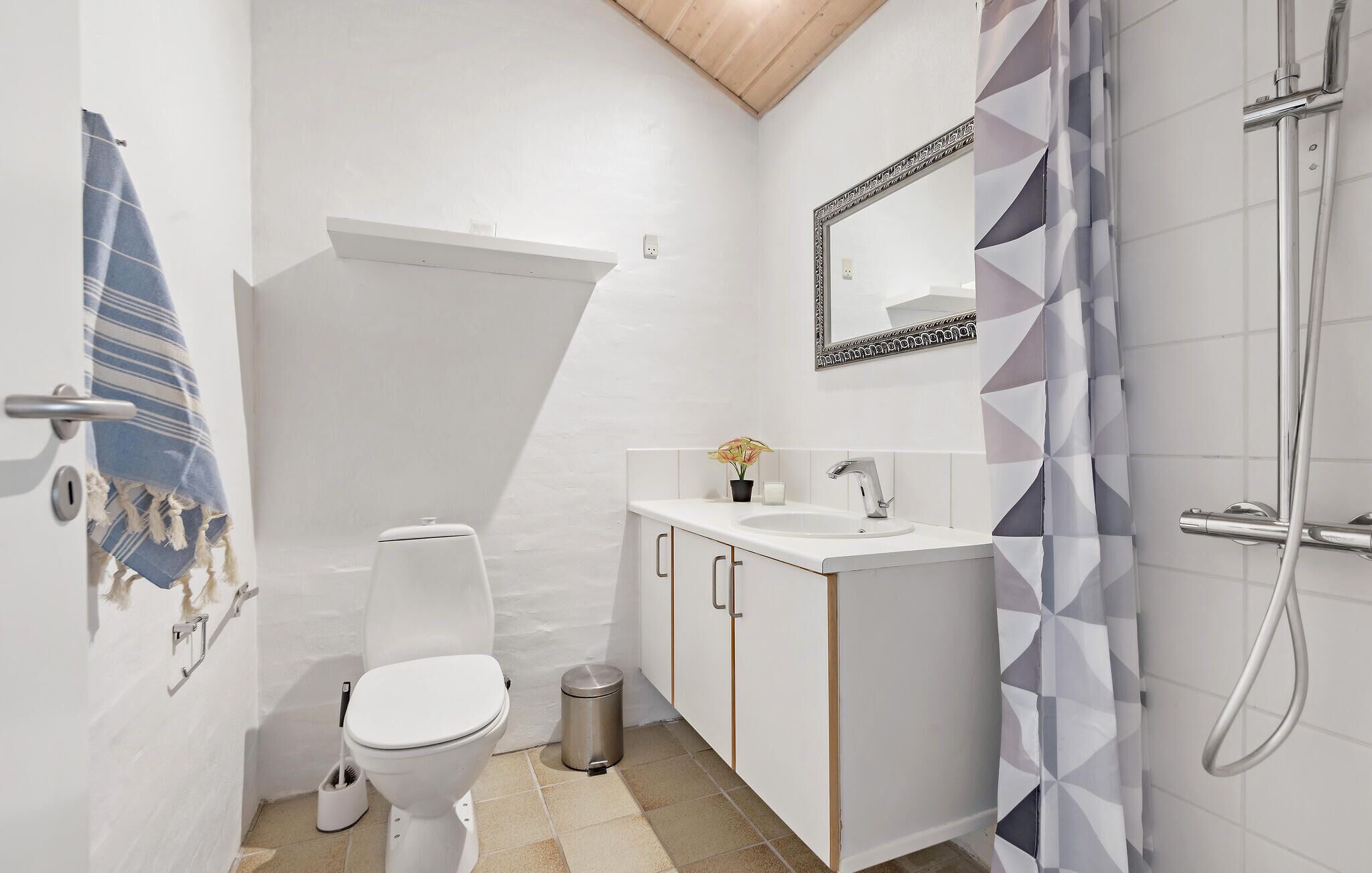 A modern bathroom with a white toilet, a sink with a mirror above it, and a shower area with a geometric-patterned curtain.