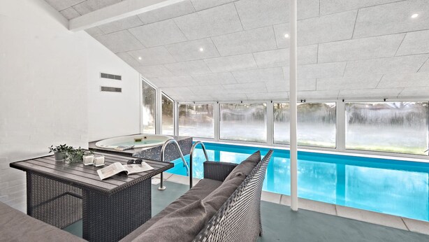 Un espace extérieur avec une piscine, une chaise longue, une table avec un journal et un jacuzzi.