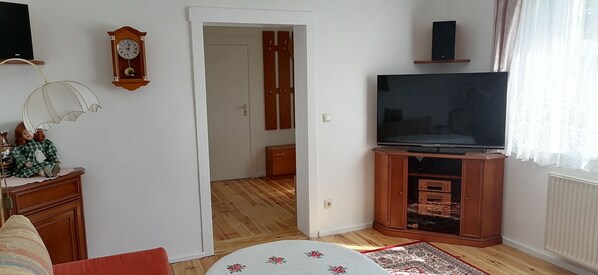 Un salon avec une télévision, une horloge et une porte qui donne sur une autre pièce.