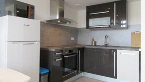 Une cuisine moderne équipée d’un réfrigérateur Brandt, d’appareils électroménagers en acier inoxydable et de meubles de rangement aux couleurs sombres.