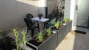 Une terrasse avec une table et des chaises, un pot de fleurs et une jardinière pleine de plantes.