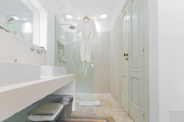Un baño moderno con un lavamanos grande de color blanco, una cabina de ducha de vidrio y un vestidor con puerta de madera.
