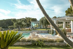 Una villa moderna con piscina, mobiliario de exterior y un pérgola.