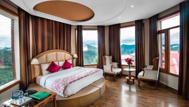 Habitación de hotel con una cama grande, dos sillones, una mesita y vistas a la montaña.