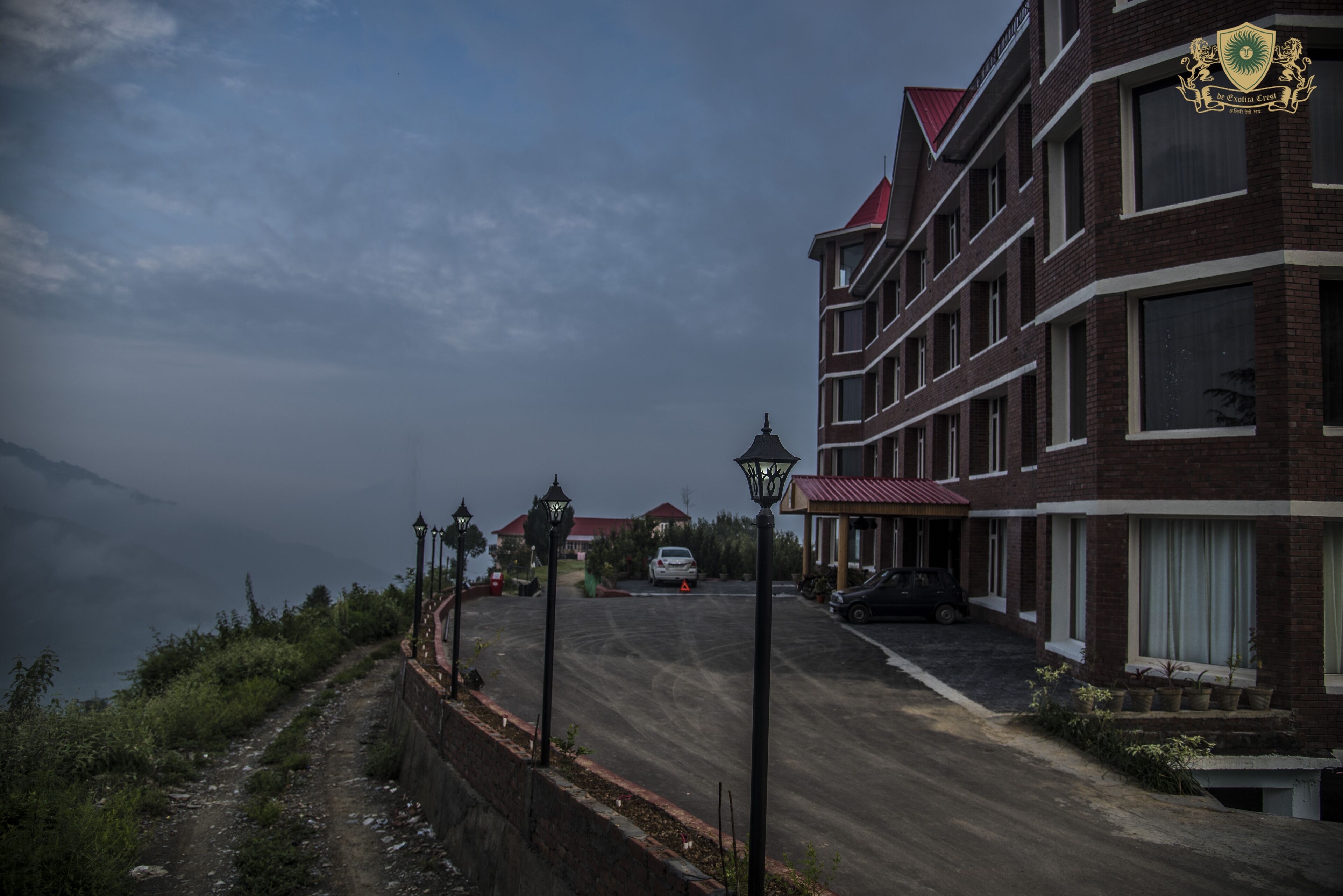 A multi-story building with a red roof, a paved driveway, and a view of a mountainous landscape.