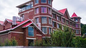 Un edificio de varios pisos con tejado rojo y fachada de ladrillo, con balcones y ventanas grandes.