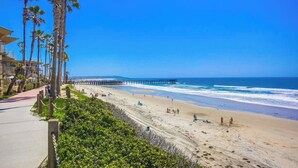 A beach with a wooden walkway, palm trees, and a pier extending into the ocean. - 11th fl. Oceanfront view plus parking and pool (San Diego)
