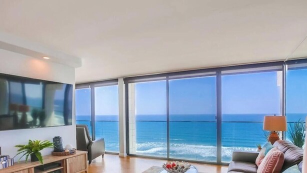 A spacious living room with a large TV, comfortable seating, and a view of the ocean. - 11th fl. Oceanfront view plus parking and pool (San Diego)