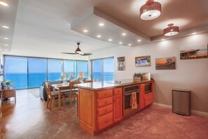 A spacious living area with a large window overlooking the ocean, a dining area with a wooden table, and a kitchen with a central island. - 11th fl. Oceanfront view plus parking and pool (San Diego)