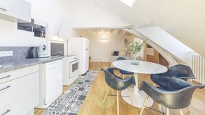 A modern kitchen with white appliances, a dining area with a round table and black chairs, and a sloped ceiling with a skylight. - Apartment Bossoreil 110m2 - Hyper center Angers (Angers)