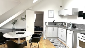 A compact kitchen with a dining area, a small dining table, and chairs. There is a microwave, a kettle, and a sink. The kitchen has white cabinets and a black countertop. - Apartment Bossoreil 110m2 - Hyper center Angers (Angers)