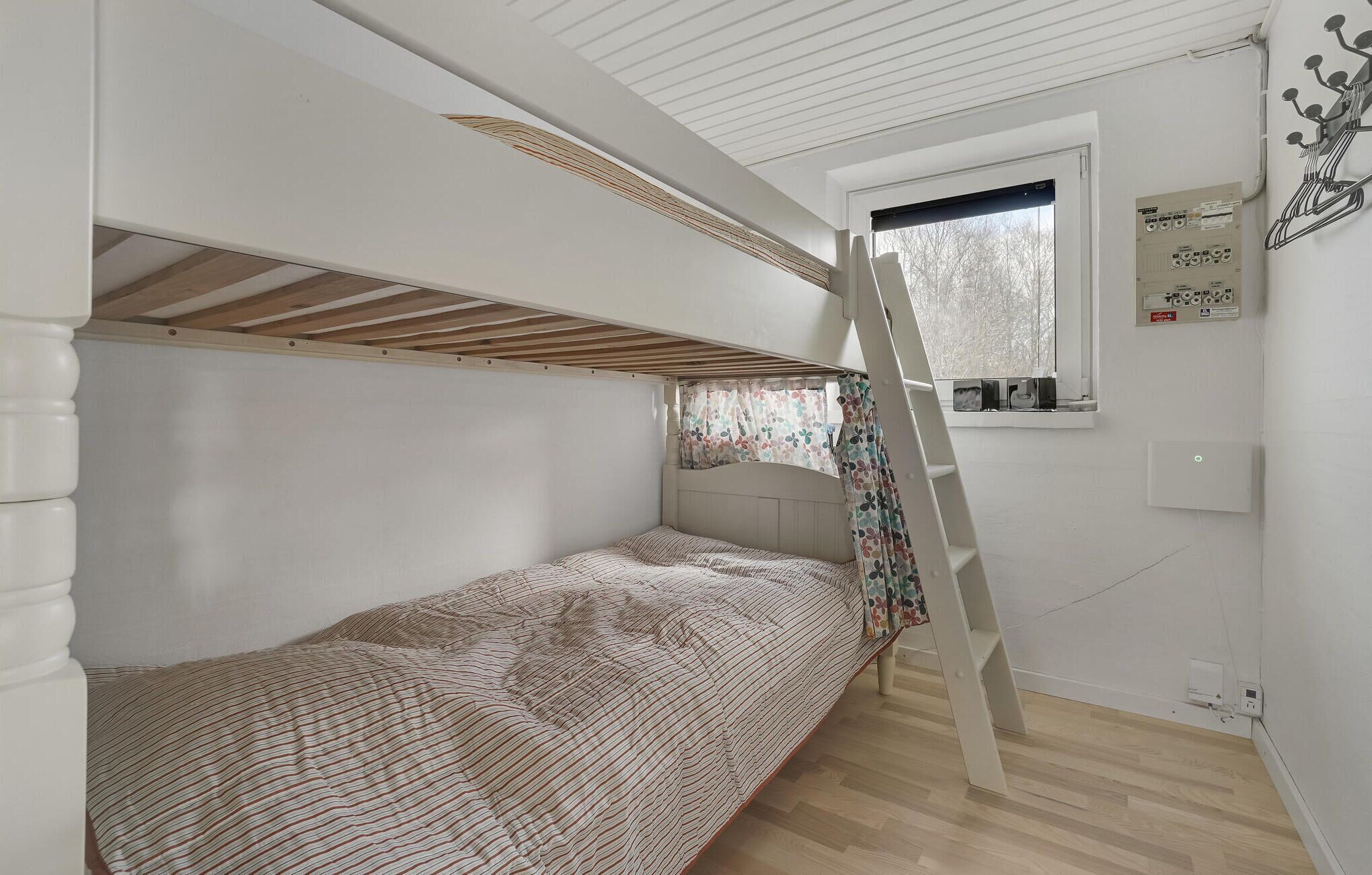 A bunk bed room with a window, wooden floor, and a ladder.