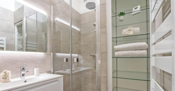 A modern bathroom with a glass shower enclosure, a vanity with a mirror, and a glass shelf with towels.