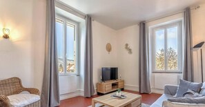 A living room with a television, a coffee table, and two windows with curtains.