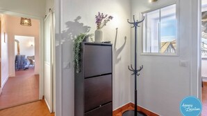 A hallway with a dark-colored cabinet, a coat rack, and a window with a view of a building. - La Savoyarde - T2 apartment close to the lake. (Menthon-Saint-Bernard)