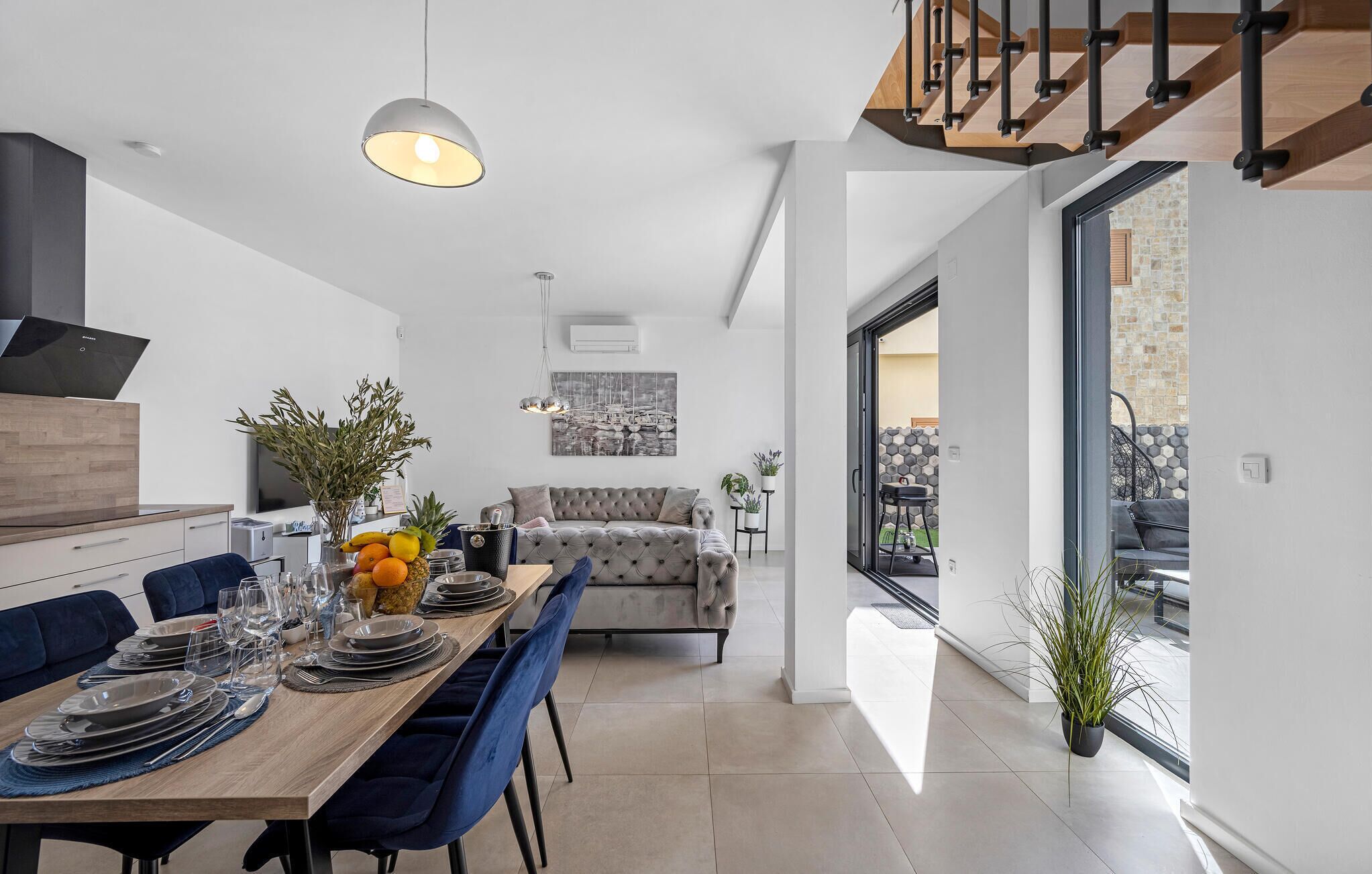 A modern kitchen with a dining area, a sofa, and a view of the outdoors.