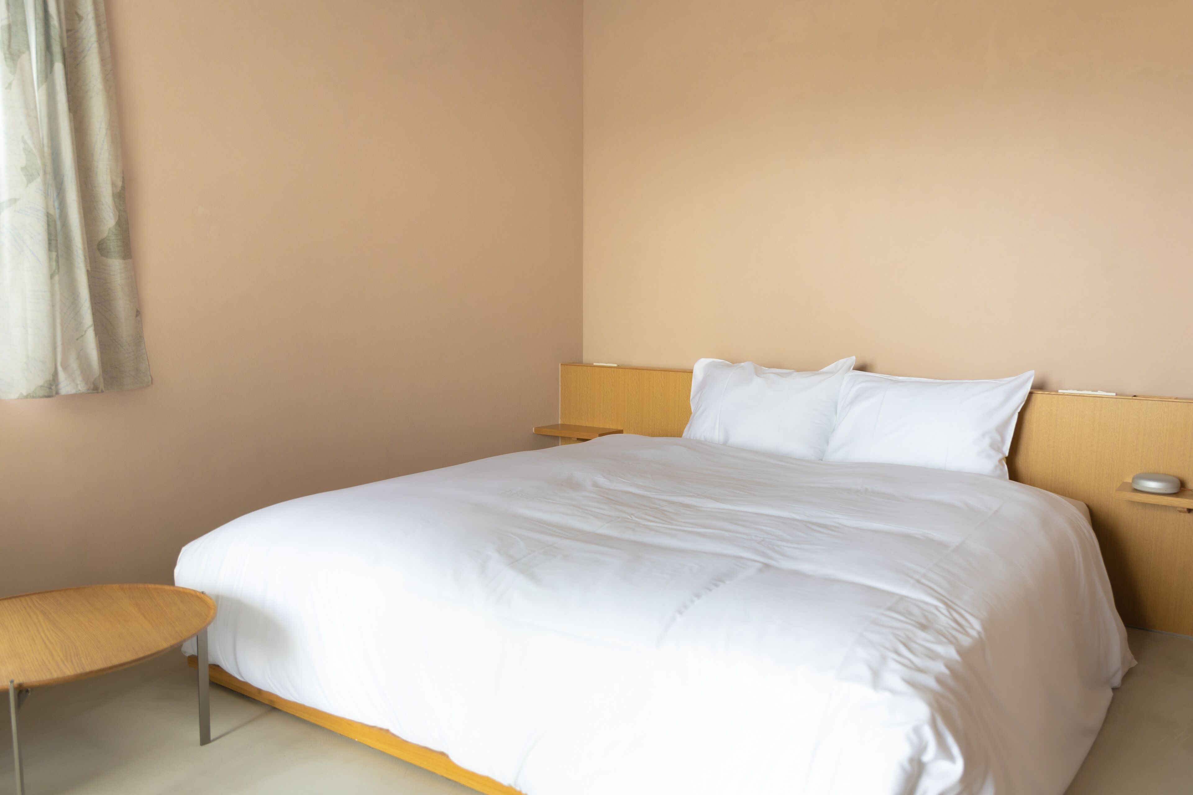 A neatly made bed with white bedding, a wooden headboard, and a bedside table with a lamp.
