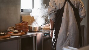 A chef in a kitchen with a stove emitting steam, cooking utensils, and a window. - Meguru Ishigaki (Ishigaki)