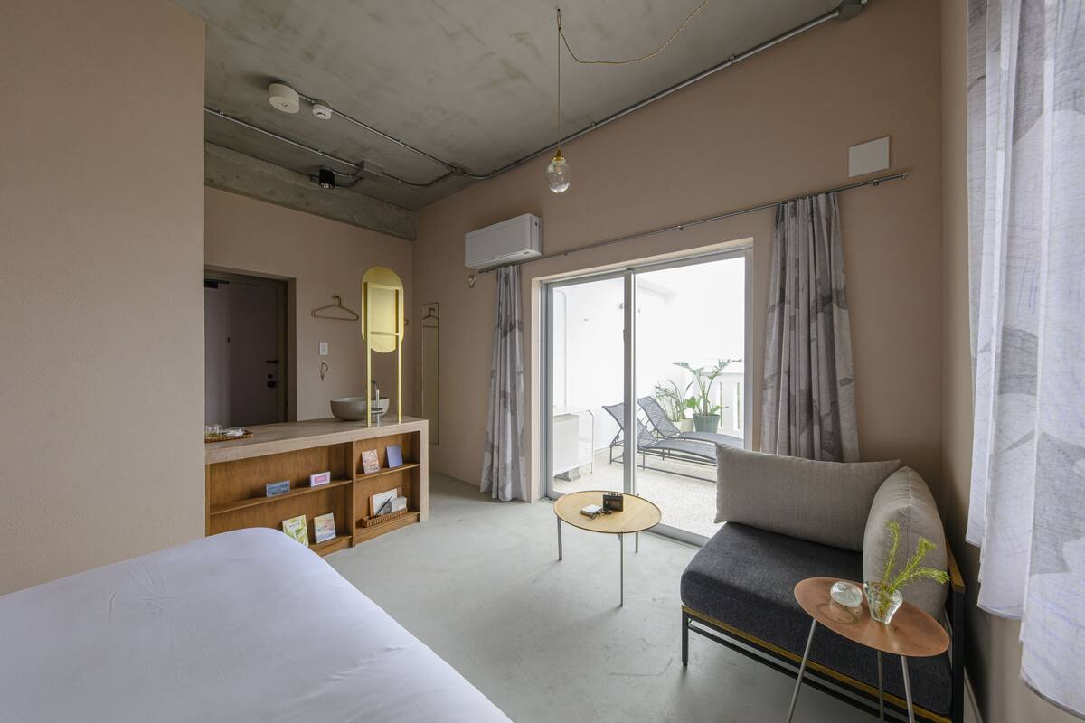 A hotel room with a bed, a sofa, a small table, a mirror, and a balcony with a view.