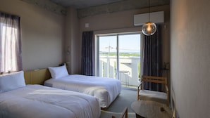 A hotel room with two beds, a small table, a chair, and a view of the outdoors. - Meguru Ishigaki (Ishigaki)