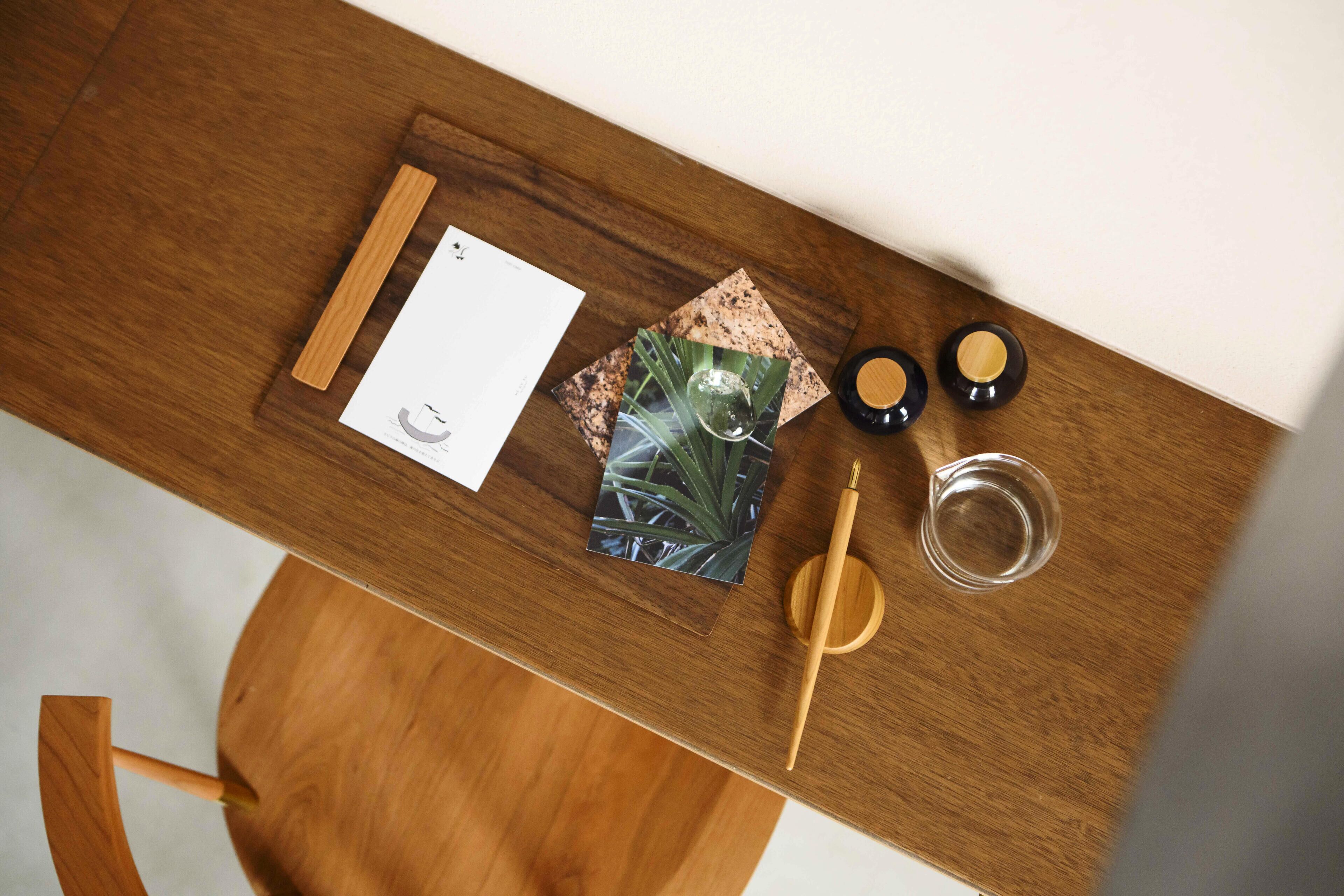 Une table en bois, une feuille de papier blanche, un stylo en bois, un verre et deux petits récipients.