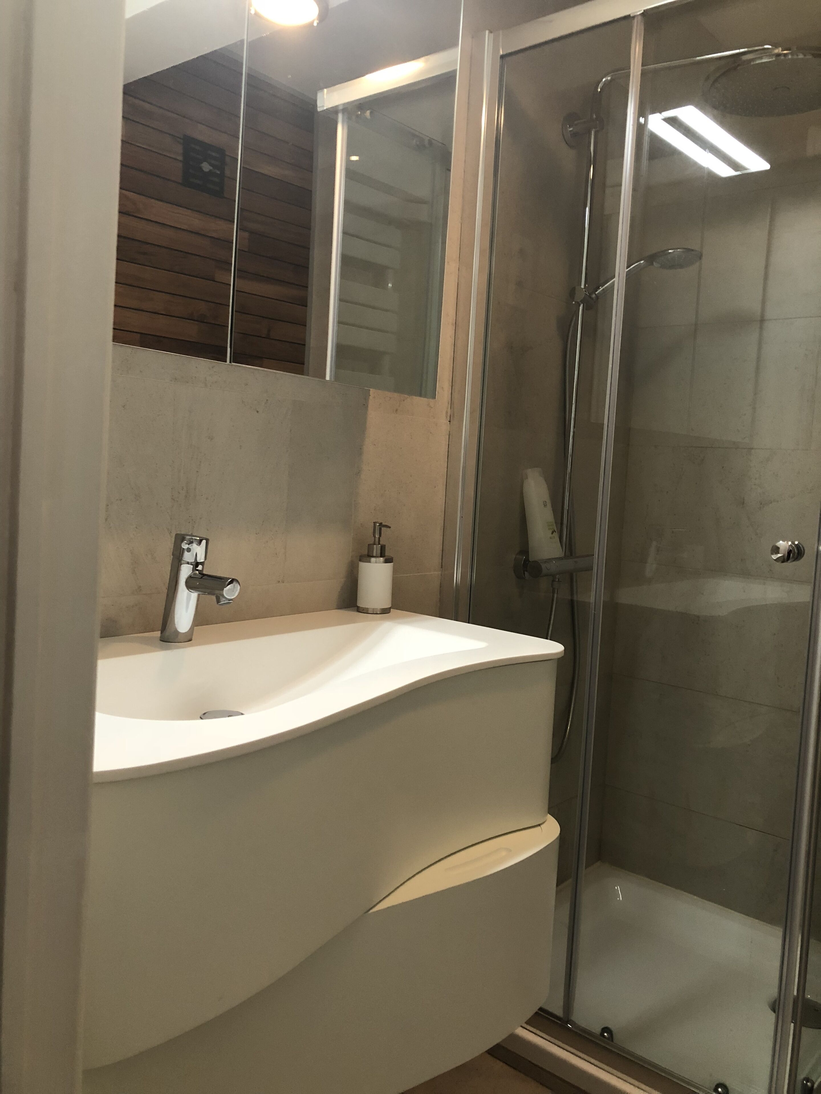 A modern bathroom with a white sink, a glass shower enclosure, and a wooden wall.