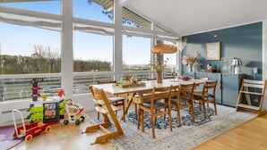 A spacious dining area with a large table and chairs, a view of the outdoors through large windows, and a kitchen area with a blue wall and modern decor. - Amazing home in Vejby with WiFi (Vejby)