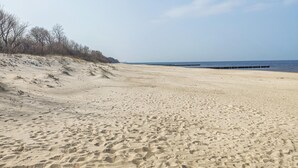 En bred, sandet strand med bløde klitter og frit udsyn til havet.