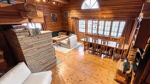 A log cabin interior with a stone fireplace, a dining area with wooden chairs, and a large window offering a view of the outdoors. - 4 bedroom beautiful home in Sälen (Sälen)