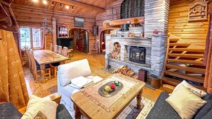 A cozy log cabin interior with a dining area, a sofa set, a fireplace, and a bookshelf. - 4 bedroom beautiful home in Sälen (Sälen)