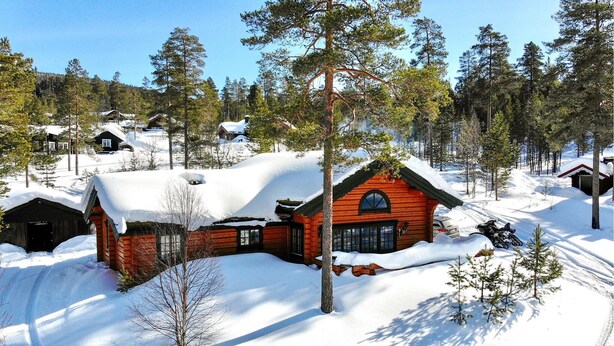 A log cabin with a snow-covered roof, surrounded by a forest and other cabins. - 4 bedroom beautiful home in Sälen (Sälen)