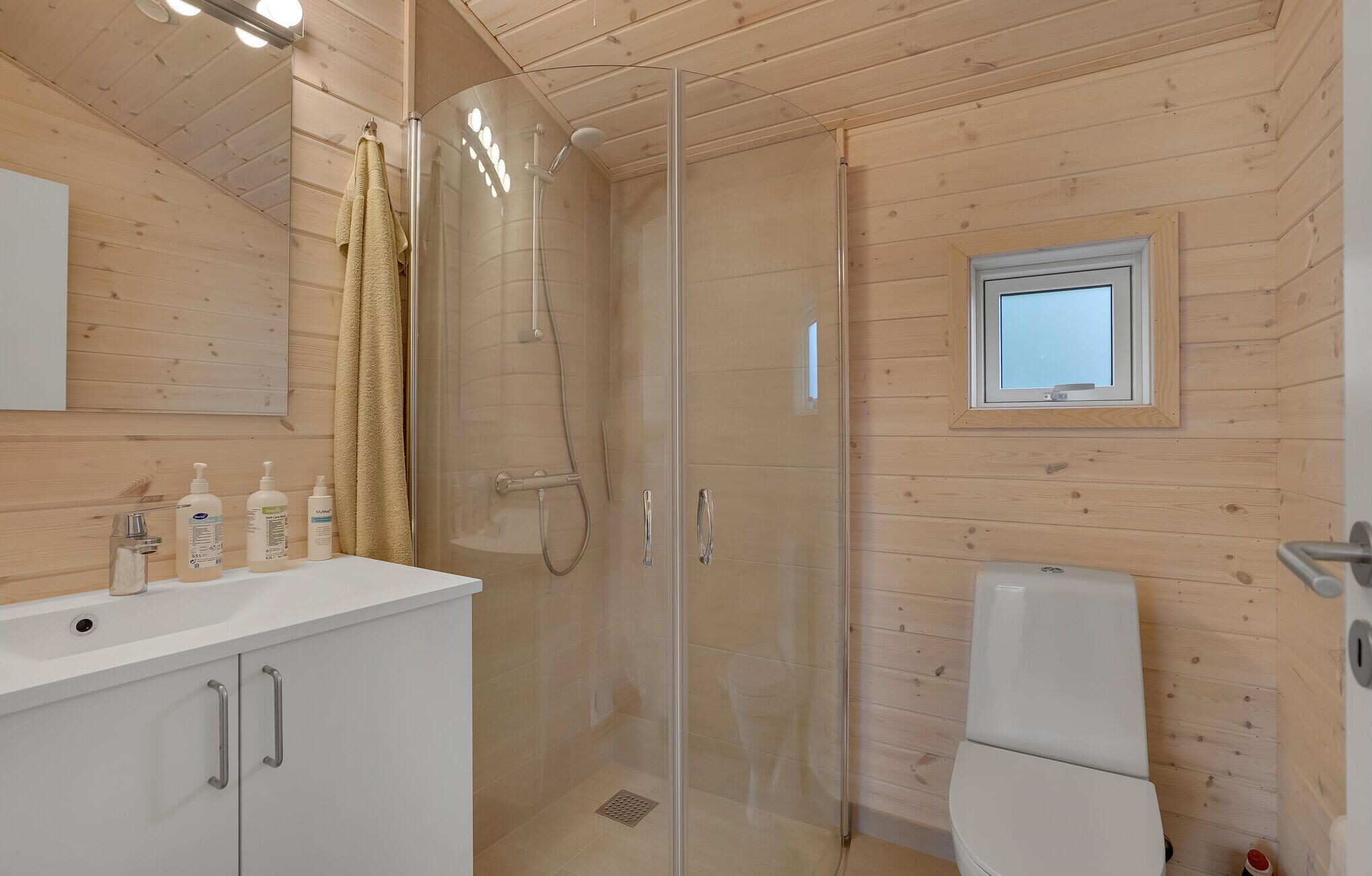 A wooden cabin bathroom with a glass shower enclosure, a toilet, and a sink with toiletries.