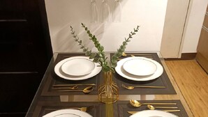 A dining table set with white plates, gold cutlery, and a vase with green foliage. - Modern minimalist condo in Davao City & very near to Samal Island (Pet Friendly) (Davao City)