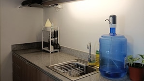 A kitchen with wooden cabinets, a granite countertop, a stainless steel sink, a large blue water dispenser, and a small potted plant. - Modern minimalist condo in Davao City & very near to Samal Island (Pet Friendly) (Davao City)