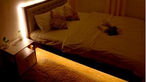 A neatly made bed with pillows, a bedside table with a lamp, and a window with curtains. - Modern minimalist condo in Davao City & very near to Samal Island (Pet Friendly) (Davao City)