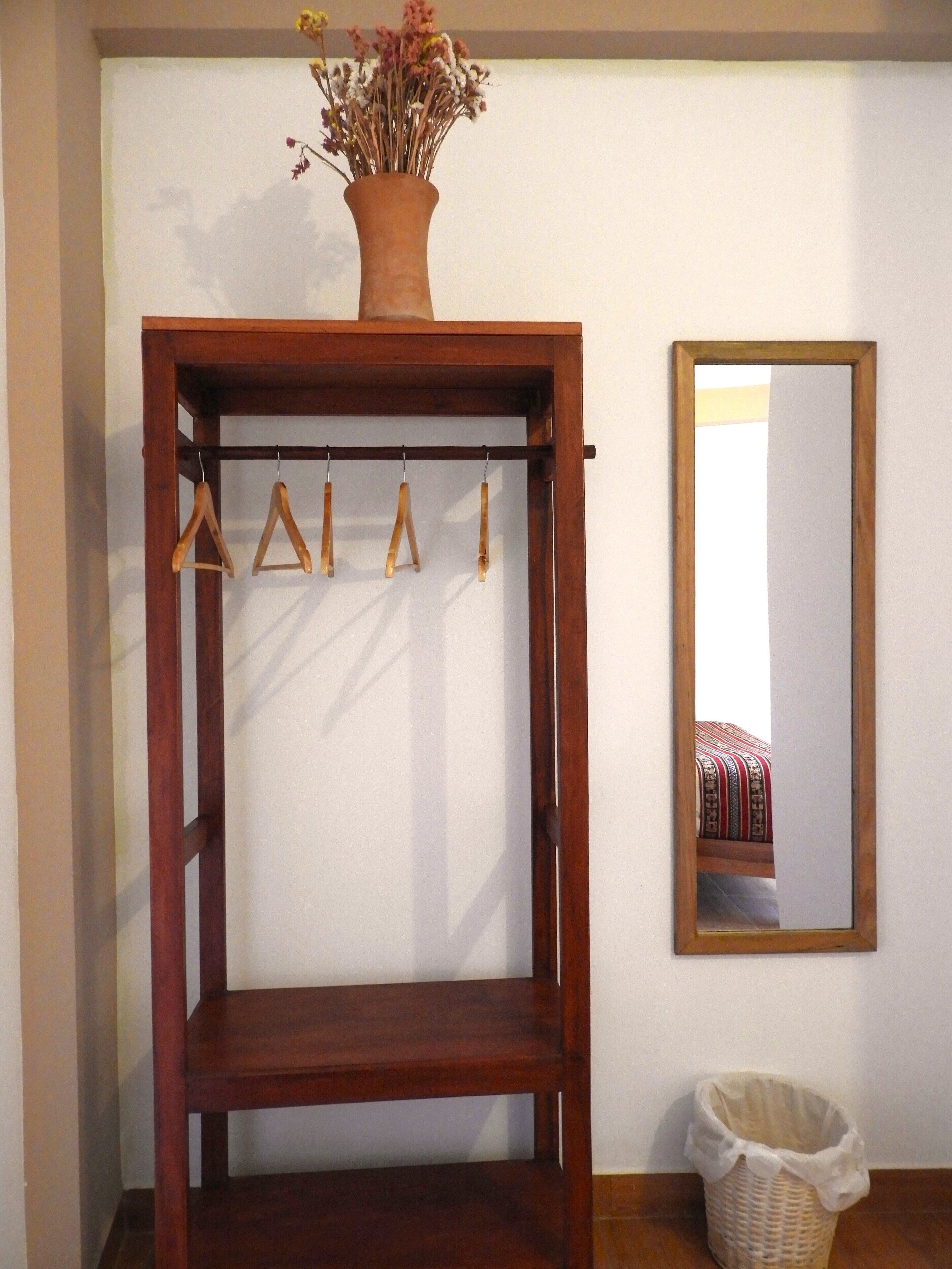 A wooden shelf with a mirror, a hanging clothes rack, and a wicker basket.